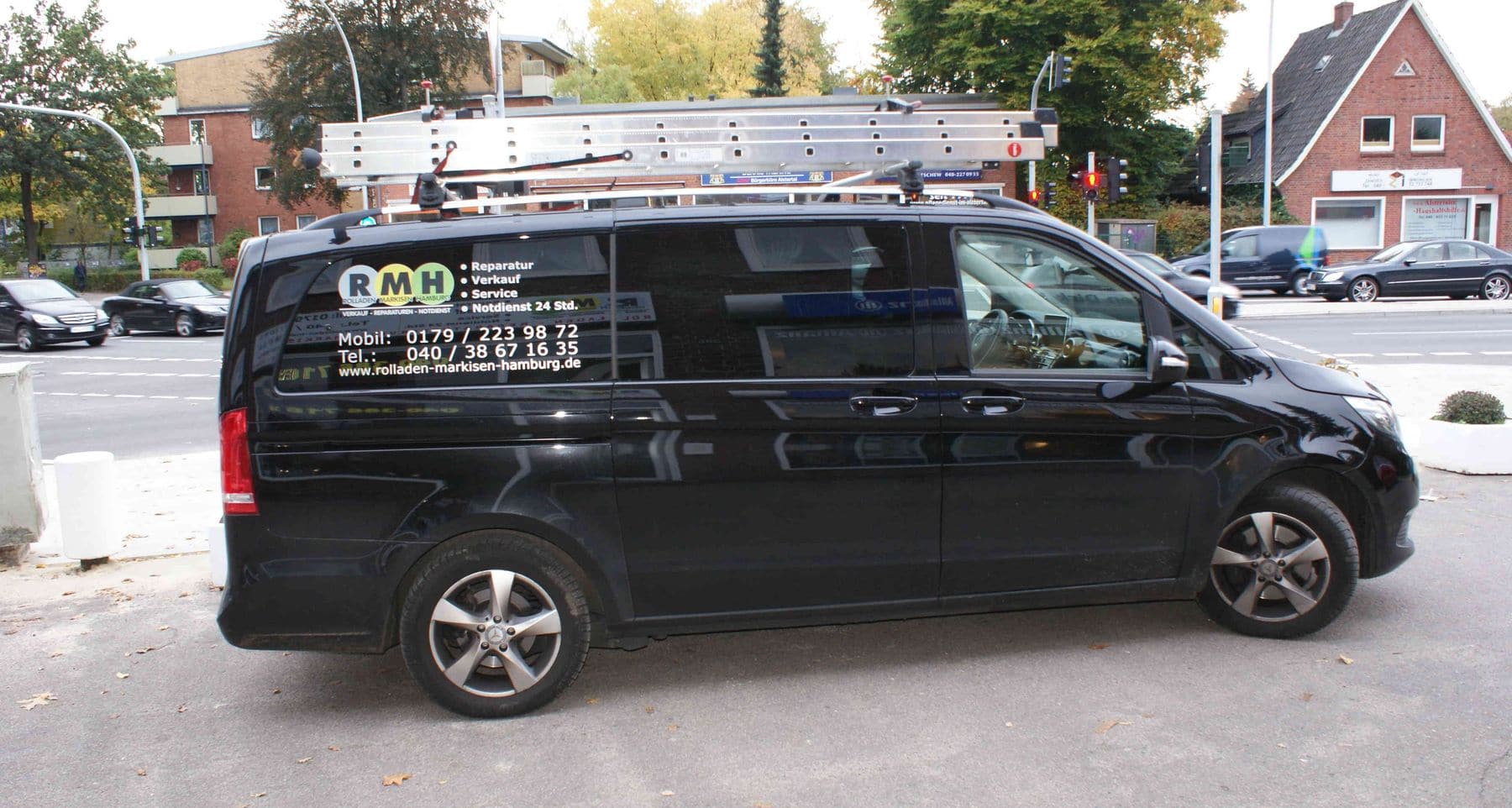 Ein schwarzer Lieferwagen mit Firmenlogos und einer auf dem Dach montierten Leiter, geparkt am Straßenrand.