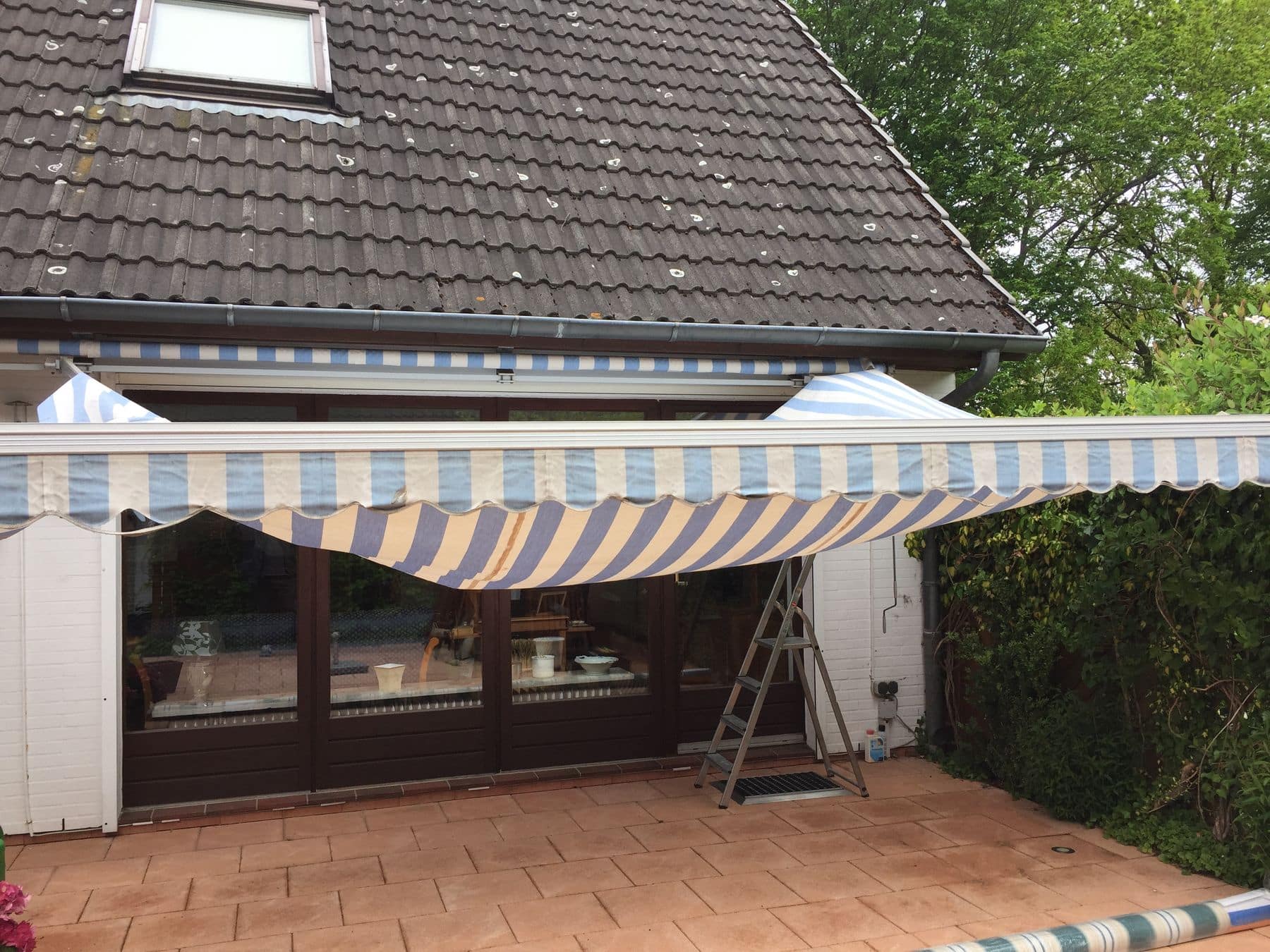 Gestreifte Markise erstreckte sich über eine Wohnterrasse mit einer am Haus angelehnten Leiter.